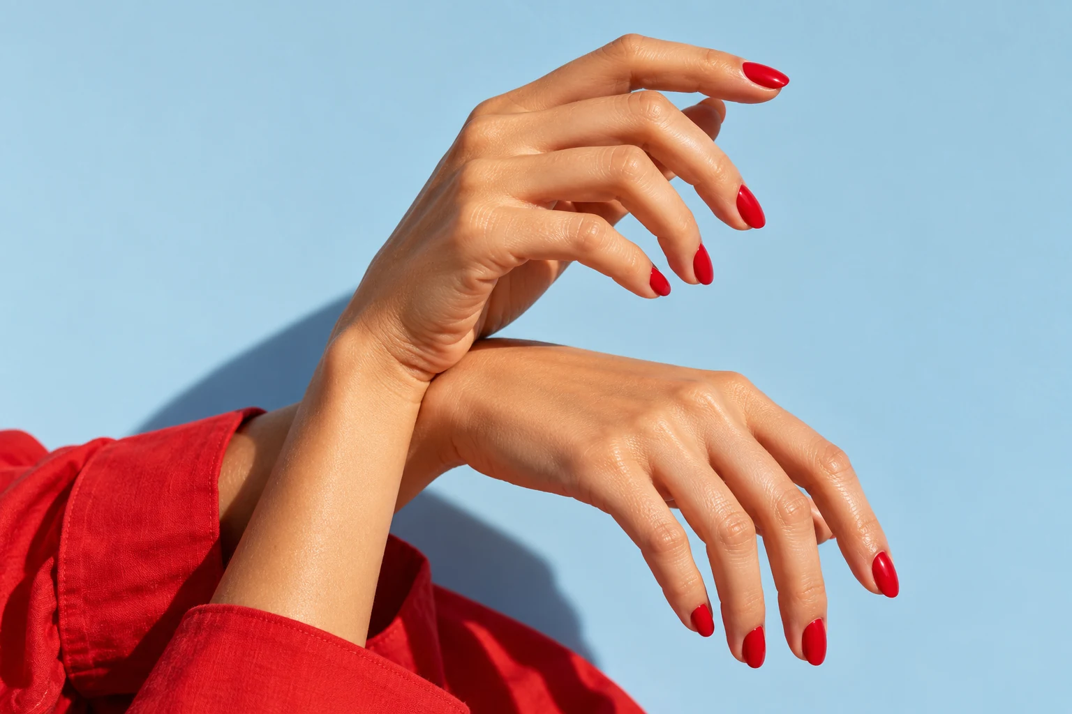 Editorial concept photograph of a glossy cherry-red manicure against pale blue